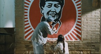 Movie still from “To Live” (1994), directed by Yimou Zhang – A man and a woman standing in front of a mural of mao zedong; Medium shot, Low angle