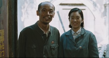 Movie still from “To Live” (1994), directed by Yimou Zhang – A man standing next to a woman in a green jacket; Medium shot, Low angle