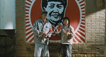 Movie still from “To Live” (1994), directed by Yimou Zhang – A man and a woman standing in front of a painting of mao zedong; Medium shot, Low angle