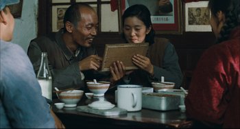 Movie still from “To Live” (1994), directed by Yimou Zhang – A man and a woman sitting at a table looking at an album; Medium shot, Over the shoulder angle