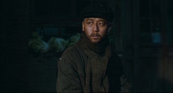 Movie still from “To Live” (1994), directed by Yimou Zhang – A man wearing a hat and a scarf in the dark; Medium shot, Low angle