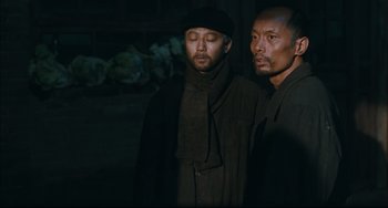 Movie still from “To Live” (1994), directed by Yimou Zhang – Two men standing next to each other in the dark; Medium shot, Over the shoulder angle