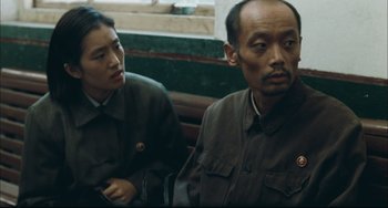 Movie still from “To Live” (1994), directed by Yimou Zhang – A man and a woman sitting next to each other on a bench; Medium shot, Over the shoulder angle