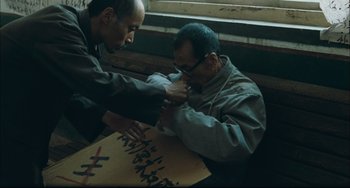 Movie still from “To Live” (1994), directed by Yimou Zhang – Two men sitting in front of a painting of chinese writing; Medium shot, High angle