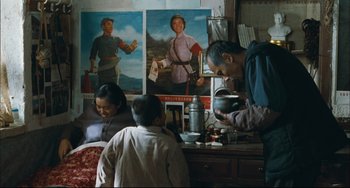 Movie still from “To Live” (1994), directed by Yimou Zhang – A man and a woman in a room with a child in front of a painting; Medium shot, Over the shoulder angle