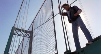 Movie still from “To Live and Die in L.A.” (1985), directed by William Friedkin – A man standing on top of a metal structure; Wide shot, Low angle