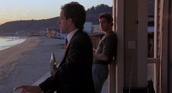 Movie still from “To Live and Die in L.A.” (1985), directed by William Friedkin – A man holding a bottle of beer next to another man leaning on a railing; Medium shot, Over the shoulder angle
