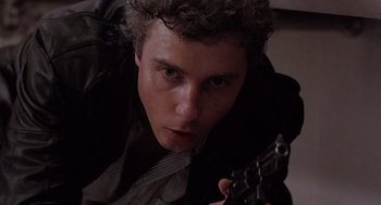 Movie still from “To Live and Die in L.A.” (1985), directed by William Friedkin – A man holding a gun in his hand and looking at the camera; Close Up shot, Low angle