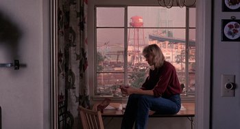 Movie still from “To Live and Die in L.A.” (1985), directed by William Friedkin – A woman sitting in front of a window looking at her cell phone; Wide shot, High angle