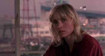 Movie still from “To Live and Die in L.A.” (1985), directed by William Friedkin – A woman with long blonde hair is looking out a window; Close Up shot, Over the shoulder angle