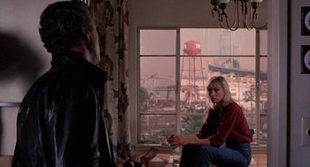 Movie still from “To Live and Die in L.A.” (1985), directed by William Friedkin – Two people sitting in front of a window with a view of a city; Wide shot, Over the shoulder angle