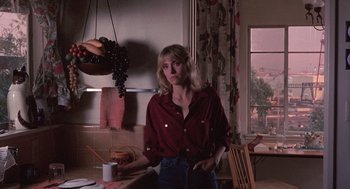 Movie still from “To Live and Die in L.A.” (1985), directed by William Friedkin – A woman standing in front of a table with a bunch of grapes on it; Medium shot, Low angle