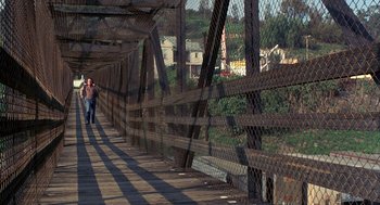 Movie still from “To Live and Die in L.A.” (1985), directed by William Friedkin – A man walking across a bridge over a river; Extreme Wide shot, High angle