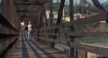 Movie still from “To Live and Die in L.A.” (1985), directed by William Friedkin – A man walking across a bridge holding onto a fence; Wide shot, High angle