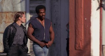 Movie still from “To Live and Die in L.A.” (1985), directed by William Friedkin – A man standing next to another man in a doorway; Medium shot, Low angle
