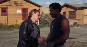 Movie still from “To Live and Die in L.A.” (1985), directed by William Friedkin – Two men shake hands in front of a building; Medium shot, Over the shoulder angle