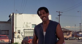 Movie still from “To Live and Die in L.A.” (1985), directed by William Friedkin – A man standing in front of a white building; Medium shot, Low angle