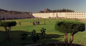 Movie still from “To Live and Die in L.A.” (1985), directed by William Friedkin – A group of people standing on top of a lush green field; Extreme Wide shot, High angle