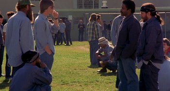 Movie still from “To Live and Die in L.A.” (1985), directed by William Friedkin – A group of people standing on top of a grass covered field; Wide shot, High angle