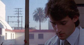 Movie still from “To Live and Die in L.A.” (1985), directed by William Friedkin – A man in a white lab coat looking out of a window; Close Up shot, Low angle
