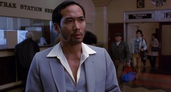 Movie still from “To Live and Die in L.A.” (1985), directed by William Friedkin – A man wearing a suit and tie standing in front of a building; Close Up shot, Low angle