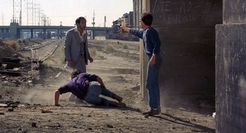 Movie still from “To Live and Die in L.A.” (1985), directed by William Friedkin – A man pointing a gun at another man laying on the ground; Wide shot, High angle