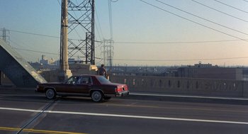 Movie still from “To Live and Die in L.A.” (1985), directed by William Friedkin – A man standing next to a car on the side of a road; Extreme Wide shot, High angle