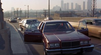 Movie still from “To Live and Die in L.A.” (1985), directed by William Friedkin – A car is parked on the side of the road; Wide shot, Over the shoulder angle