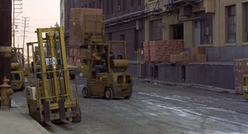 Movie still from “To Live and Die in L.A.” (1985), directed by William Friedkin – A fork lift is driving down the street; Wide shot, High angle