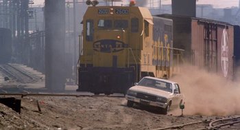Movie still from “To Live and Die in L.A.” (1985), directed by William Friedkin – A train and a car on a dirt road; Extreme Wide shot, Low angle