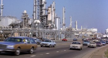 Movie still from “To Live and Die in L.A.” (1985), directed by William Friedkin – Cars driving down a highway near an oil refinery; Extreme Wide shot, Low angle