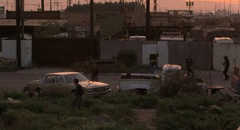 Movie still from “To Live and Die in L.A.” (1985), directed by William Friedkin – A group of people standing next to a truck; Extreme Wide shot, High angle