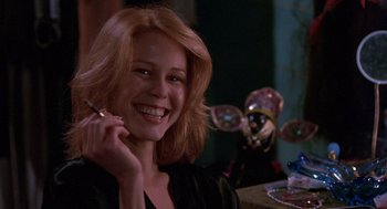 Movie still from “To Live and Die in L.A.” (1985), directed by William Friedkin – A woman smiles while holding a pen in her mouth; Close Up shot, Low angle