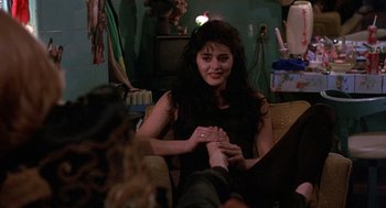 Movie still from “To Live and Die in L.A.” (1985), directed by William Friedkin – A woman sitting on a couch holding a man's hand; Medium shot, High angle