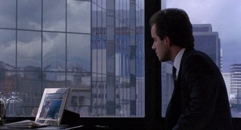 Movie still from “To Live and Die in L.A.” (1985), directed by William Friedkin – A man sitting at a desk looking at a laptop; Medium shot, Over the shoulder angle