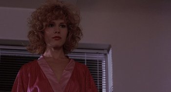 Movie still from “To Live and Die in L.A.” (1985), directed by William Friedkin – A woman in a red dress standing next to a window; Close Up shot, Low angle
