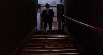Movie still from “To Live and Die in L.A.” (1985), directed by William Friedkin – A man in a suit standing in front of a staircase; Wide shot, Low angle