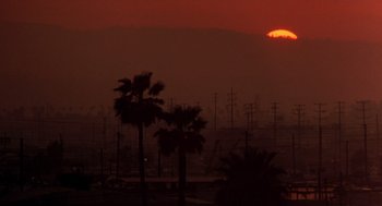 Movie still from “To Live and Die in L.A.” (1985), directed by William Friedkin – The sun is setting over a city filled with power lines and palm trees; Extreme Wide shot, Low angle