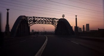 Movie still from “To Live and Die in L.A.” (1985), directed by William Friedkin – A view of an overpass at dusk with a car driving on it; Extreme Wide shot, Low angle