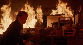 Movie still from “To Live and Die in L.A.” (1985), directed by William Friedkin – A man standing in front of a fire in a room; Medium shot, Low angle
