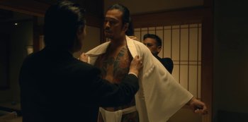 Movie still from “Tokyo Vice” (2022), created by J.T. Rogers – A man with a tattoo on his chest is getting his shirt undone; Medium shot, Low angle