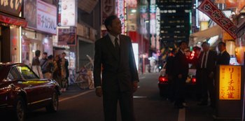 Movie still from “Tokyo Vice” (2022), created by J.T. Rogers – A man wearing a suit and tie standing on a street; Medium shot, Low angle