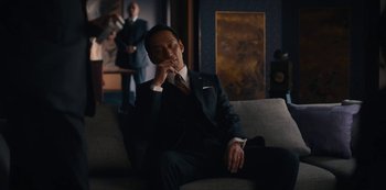 Movie still from “Tokyo Vice” (2022), created by J.T. Rogers – A man in a suit sitting on a couch in a room; Medium shot, Low angle