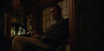 Movie still from “Tokyo Vice” (2022), created by J.T. Rogers – A man sitting in front of a window holding a nintendo wii game controller; Medium shot, Low angle