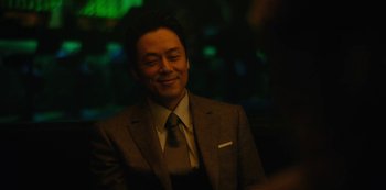 Movie still from “Tokyo Vice” (2022), created by J.T. Rogers – A man wearing a suit and tie smiling; Close Up shot, Over the shoulder angle