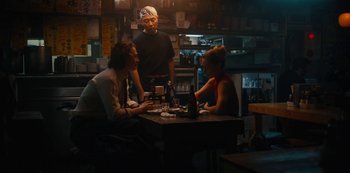 Movie still from “Tokyo Vice” (2022), created by J.T. Rogers – Three people sitting at a table in front of a bartender; Medium shot, Over the shoulder angle