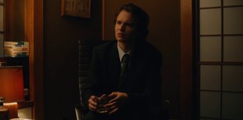 Movie still from “Tokyo Vice” (2022), created by J.T. Rogers – A man in a suit sitting in a black chair; Medium shot, Low angle