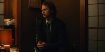 Movie still from “Tokyo Vice” (2022), created by J.T. Rogers – A man in a suit and tie sitting in a chair; Medium shot, Low angle