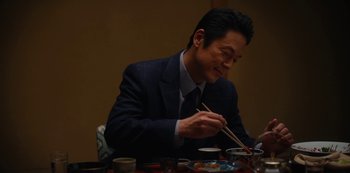 Movie still from “Tokyo Vice” (2022), created by J.T. Rogers – A man sitting at a table with chopsticks in front of a bowl; Medium shot, Over the shoulder angle