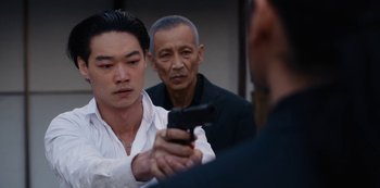 Movie still from “Tokyo Vice” (2022), created by J.T. Rogers – A man holding a gun in front of two other men; Close Up shot, Over the shoulder angle